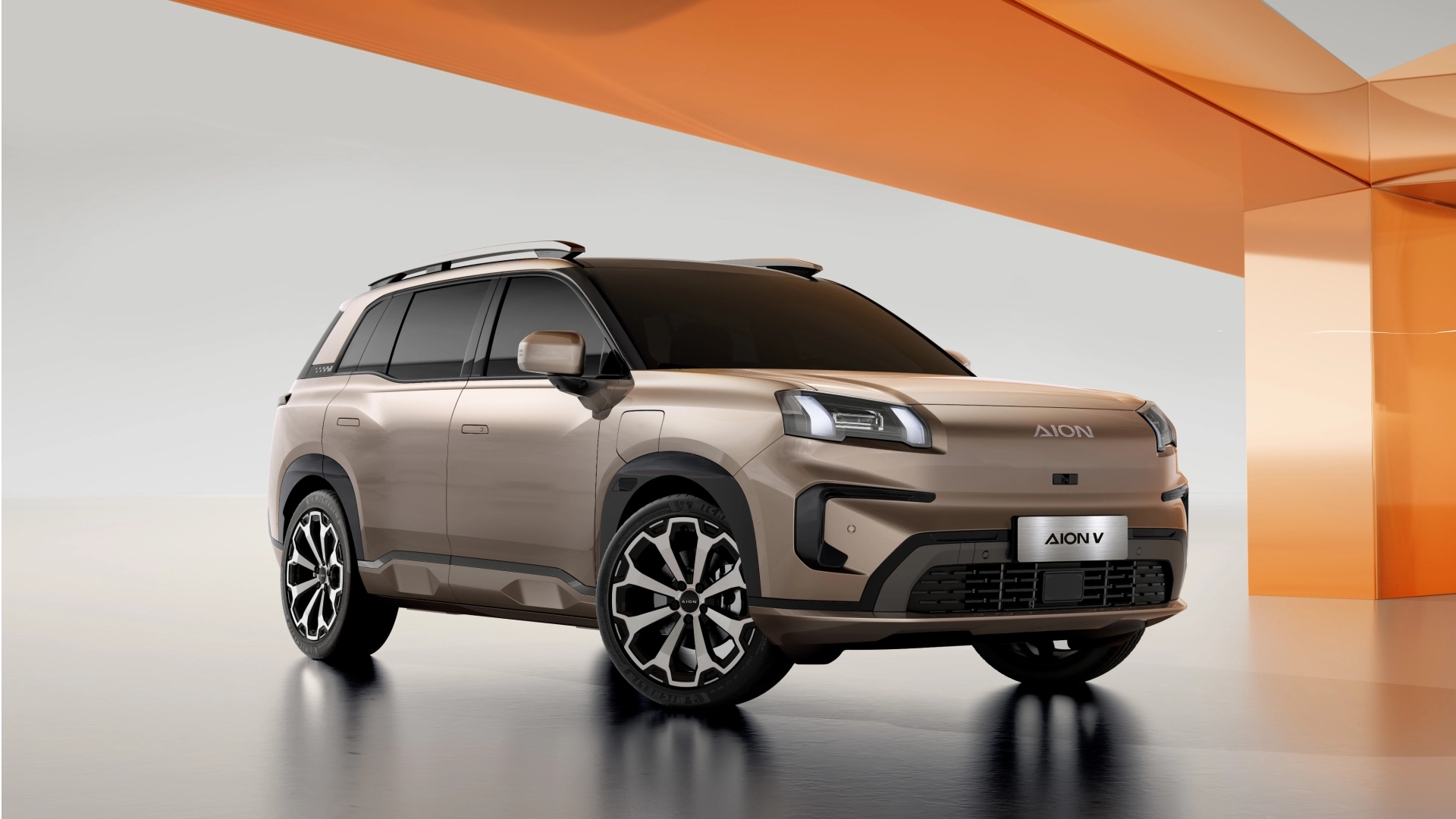 Beige GAC AION V viewed from the front three-quarter angle in an orange architectural studio